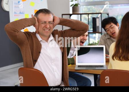 Reifer Geschäftsmann, der unter lauten Kollegen im Büro leidet Stockfoto