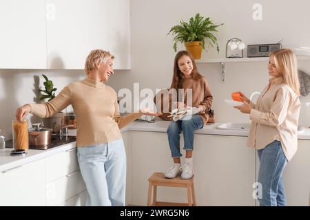 Kleines Mädchen mit Mutter und Großmutter, das Geschirr in der Küche wäscht Stockfoto