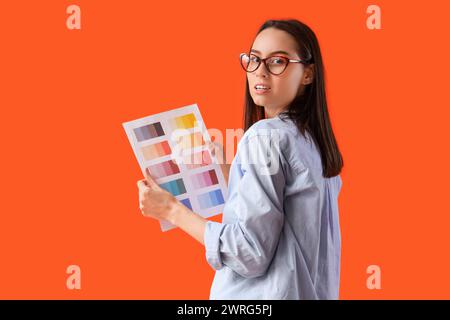 Weibliche Designerin in Brille mit Farbpaletten auf orangem Hintergrund Stockfoto