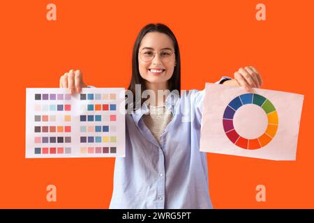 Weibliche Designerin in Brille mit Farbpaletten auf orangem Hintergrund Stockfoto