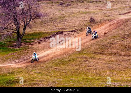 Drei Personen genießen die Erholung im Freien, indem sie mit dem Dirt Bike durch eine Grünlandanlage auf einer Feldstraße in der natürlichen Landschaft fahren Stockfoto