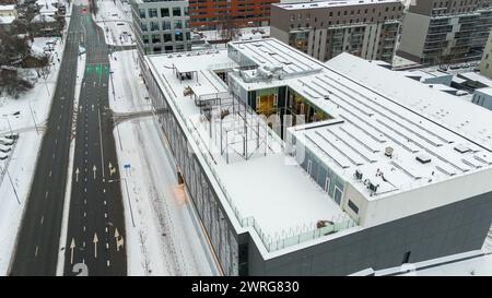 Drohnenfotos von einem kleinen Basketballfeld, Bänken und einem Ort zum Entspannen auf einem Dach, bedeckt von Schnee während des bewölkten Wintertages Stockfoto