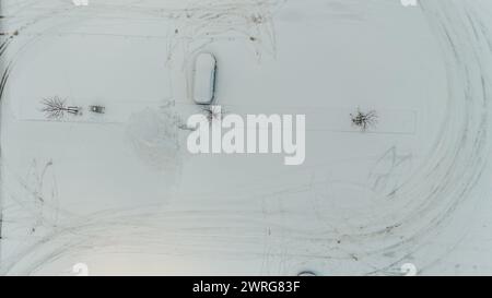 Drohnenfotografie eines leeren Parkplatzes und eines schneebedeckten Autos während des bewölkten Wintertages Stockfoto