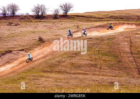 Eine Gruppe von Menschen fährt Dirt Bikes auf einem Feldweg in einer grasbewachsenen Landschaft, umgeben von Pflanzengemeinschaften und natürlichen Hängen Stockfoto