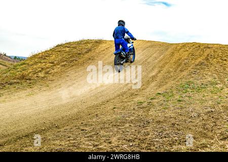 Ein Motocross-Enthusiast mit Helm fährt mit seinem Motorrad auf einer unbefestigten Straße und schleudert mit seinen Reifen Staub, während er durch den offenen Himmel rastet Stockfoto