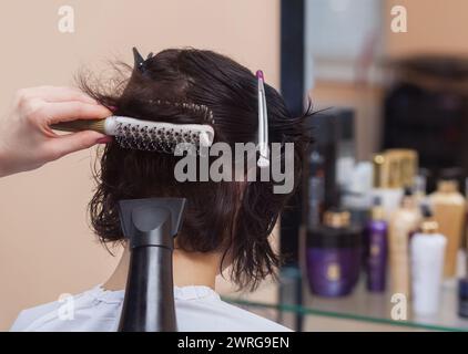 Die Friseurin trocknet ihr Haar als Brünette in einem Schönheitssalon. Stockfoto