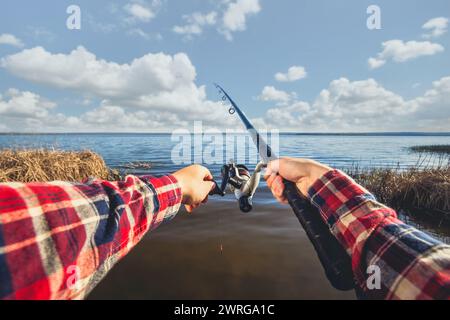 Der Fischer fängt Fische am Ufer des Sees, hält seine Hände drehend gegen den wunderschönen See und den bewölkten Himmel. Stockfoto