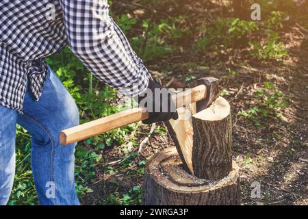 Männlicher Holzfäller im schwarz-weißen karierten Hemd mit einer Axt, die einen Baum im Wald hackt. Stockfoto