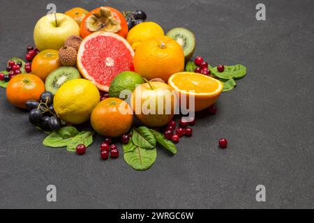 Verschiedene exotische Früchte in verschiedenen Farben. Mandarinen, Grapefruit, Litschi, Kiwi und Trauben mit Mangold-Blättern. Schwarzer Hintergrund. Kopierbereich von oben Stockfoto