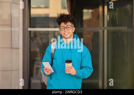 Der Schüler macht eine Kaffeepause und stöbert auf dem Smartphone in der Stadt Stockfoto