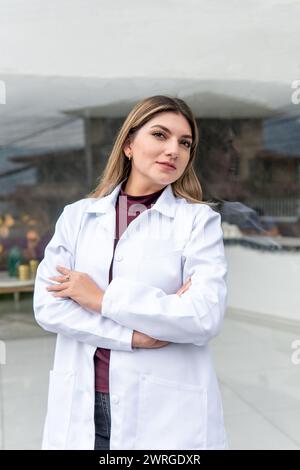 Vertikales Porträt eines jungen Latina-Arztes mit blondem Haar und weißem Fell draußen mit überkreuzten Armen Stockfoto