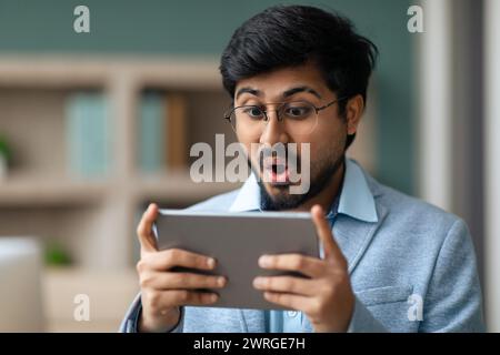 Begeisterter Hindu-Unternehmer, der ein digitales Tablet am modernen Arbeitsplatz verwendet Stockfoto