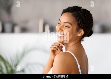 Glückliche junge schwarze Frau mit weißem Tanktop, lächelnd und berührend am Kinn Stockfoto