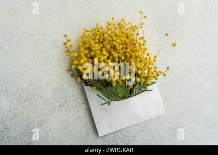 Blick von oben auf einen Haufen gelber Mimosa-Blüten in einem Umschlag auf einem Tisch Stockfoto