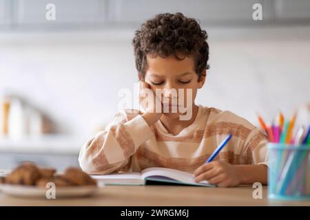 Kleiner schwarzer Junge, der sich müde und schläfrig fühlt, während er seine Hausaufgaben macht Stockfoto