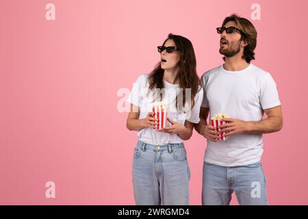 Überraschte Mann und Frau in lässigen weißen T-Shirts und Jeans mit Popcorn Stockfoto