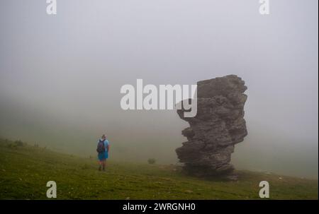 Silhouette eines Mannes, der an einem großen Felsen durch den Nebel im Berg vorbeigeht. Sharr Mountains, Popova Shapka. Stockfoto