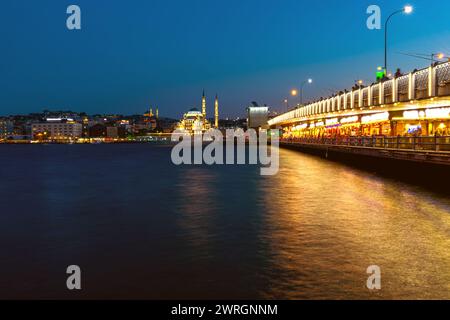 Abendlicher Blick auf die galata-Brücke mit leuchtenden Lichtern und die Silhouette von istanbul vor dem Abendhimmel mit der neuen Moschee Yeni Cami. Stockfoto