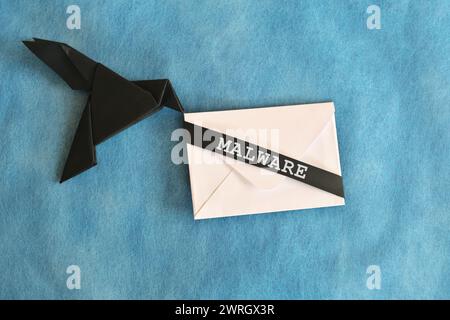 Origami aus schwarzem Rabenpapier mit weißem Briefumschlag mit Wort-Malware. E-Mail-Konzept für Malware-Angriffe. Stockfoto