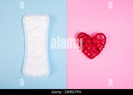 Sanitärkissen und rotes Herz auf farbigem Hintergrund. Menstruation und Frauengesundheitskonzept. Stockfoto