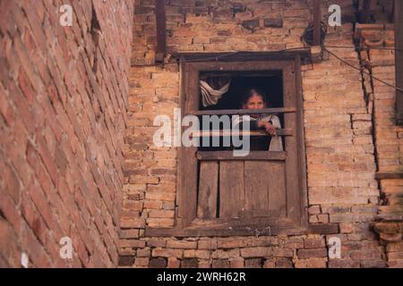 KATHMANDU, NEPAL - 06. NOVEMBER 2006: Die alte Frau beobachtet von einem Fenster eines Hauses auf der Straße der Altstadt im Kathmandu Valley, Nepal. Stockfoto