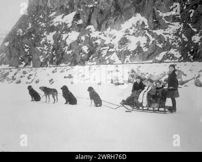 Reisen mit dem Hundeschlitten, zwischen 1900 und 1917. Das Hundeschlittenteam war an einem Schlitten mit vier Mädchen vor einer schneebedeckten Klippe angelehnt. Stockfoto