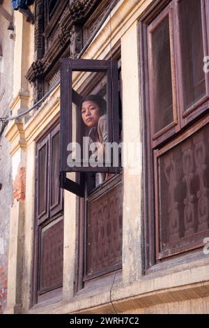 KATHMANDU, NEPAL - 6. NOVEMBER 2006: Die Frau beobachtet aus einem Fenster eines Hauses auf der Straße der Altstadt im Kathmandu Valley, Nepal. Stockfoto