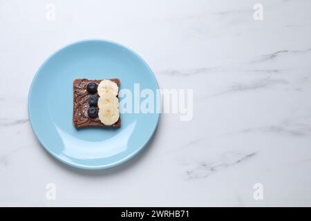 Toast mit leckerer Nussbutter, Heidelbeeren, Banane und Nüssen isoliert auf weißem Marmortisch, Blick von oben. Leerzeichen für Text Stockfoto