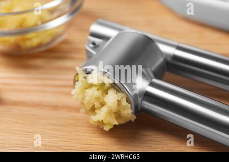 Eine Metallpresse mit zerdrücktem Knoblauch auf Holztisch, Großaufnahme Stockfoto