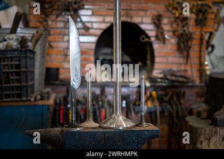 Die Klinge und Rohlinge zum Schmieden eines Messers auf einem Amboss vor dem Hintergrund eines Hochofens in einer Schmiede. Die traditionelle Methode zum Schmieden von Messern in Stockfoto