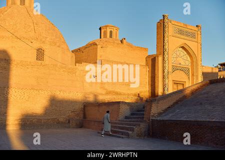 Blick auf den Kulturplatz und die kalyanische Minaretmoschee masjid Madrasah bei Sonnenuntergang und einheimischer Mann, der auf der Treppe in Buchara, Usbekistan, spaziert Stockfoto