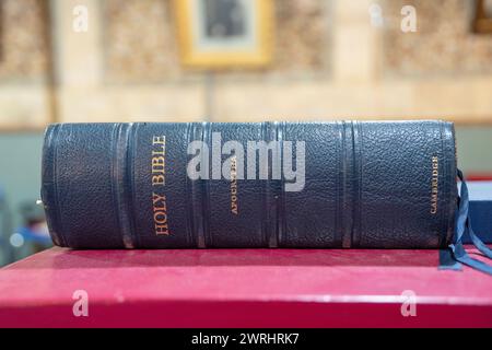 Heilige Bibel aus schwarzem Vintage-Leder mit goldener Apokryphen-Inschrift, ausgestellt auf einem Karmesinpult Stockfoto