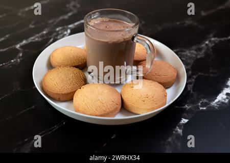 Eine luxuriöse Szene mit einer dampfenden Tasse heißer Schokolade neben einem Teller köstlicher Kekse auf einer schicken schwarzen Marmoroberfläche Stockfoto
