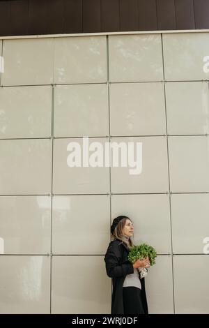 Eine Frau steht vor einer Wand und hält einen Haufen frisches Gemüse in der Hand. Vertikales Bild. Stockfoto