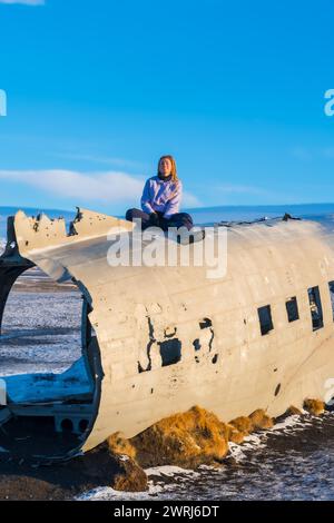 Frau, die auf Solheimasandur sitzt, lächelt vor der Meditation in Island Stockfoto