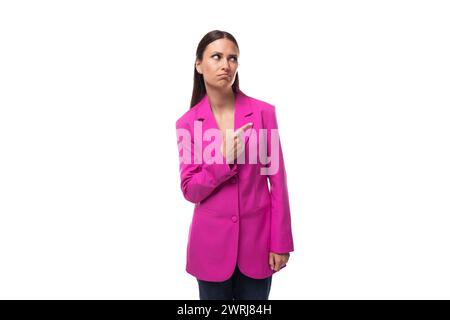 Eine junge, kluge Büroangestellte mit schwarzen Haaren in einer rosa Jacke steht nachdenklich Stockfoto
