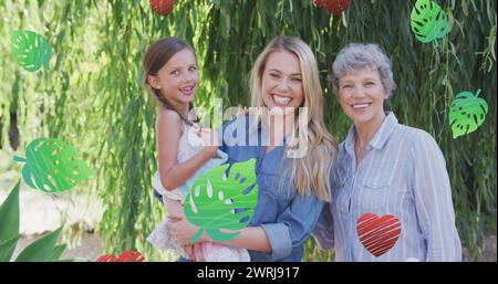 Bild von Herzen und Blättern über lächelnden kaukasischen Mehrgenerationsfrauen im Garten Stockfoto