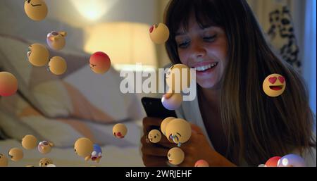 Junge Frau lächelt mit dem Smartphone, während Emoji-Symbole in 4 km vorbeifliegen. Stockfoto