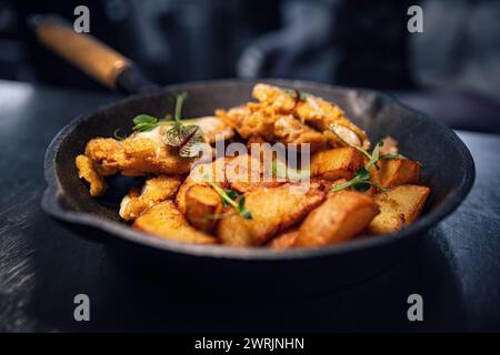 Gebratene Kartoffelscheiben mit Schnitzel, serviert in einer Eisenpfanne, Nahaufnahme Stockfoto
