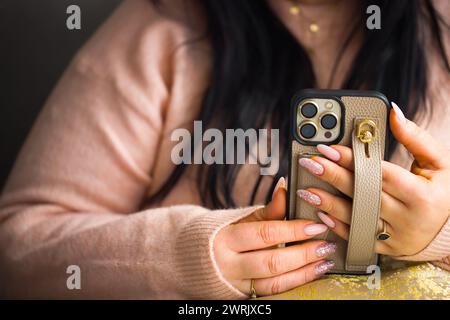 Eine Nahaufnahme der Hände einer Frau, die ein Smartphone hält. Die Frau hat atemberaubende pinkfarbene Gelnägel, sorgfältig bemalt mit zwei Nägeln, die mit Stiften verziert sind Stockfoto