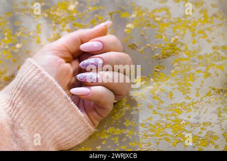 Eine sorgfältig gepflegte Frauenhand mit atemberaubenden rosa Gel-Nägeln. Die Nägel sind perfekt bemalt, zwei sind mit stilvollen, mehrfarbigen Farben verziert Stockfoto