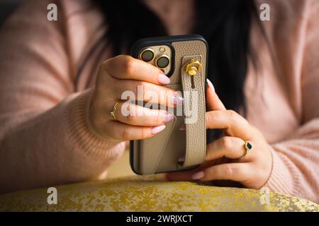 Eine Nahaufnahme der Hände einer Frau, die ein Smartphone hält. Die Frau hat atemberaubende pinkfarbene Gelnägel, sorgfältig bemalt mit zwei Nägeln, die mit Stiften verziert sind Stockfoto