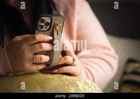 Eine Nahaufnahme der Hände einer Frau, die ein Smartphone hält. Die Frau hat atemberaubende pinkfarbene Gelnägel, sorgfältig bemalt mit zwei Nägeln, die mit Stiften verziert sind Stockfoto
