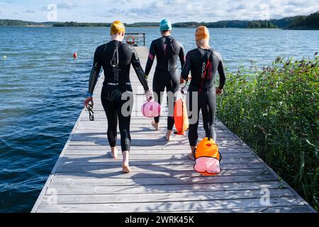 FREIWASSERSCHWIMMER, Åland, OSTSEE: Drei Frauen, die sich auf dem Weg zum Freiwasserschwimmen auf Åland in der Ostsee mit aufblasbaren Bouys zum Schutz vor Schiff- und Bootsverkehr machen. Das Schwimmen im offenen Wasser ist eine Form des Schwimmens, das in natürlichen Gewässern wie Seen, Flüssen und Ozeanen statt in einem Pool stattfindet. Sie erfordert im Vergleich zum Schwimmbadschwimmen andere Fähigkeiten und Techniken sowie eine höhere geistige und körperliche Belastbarkeit aufgrund der unterschiedlichen Wasserbedingungen und der potenziellen Anwesenheit von Wildtieren und Bootstouren. Stockfoto