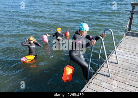 FREIWASSERSCHWIMMER, Åland, OSTSEE: Drei Frauen, die sich auf dem Weg zum Freiwasserschwimmen auf Åland in der Ostsee mit aufblasbaren Bouys zum Schutz vor Schiff- und Bootsverkehr machen. Das Schwimmen im offenen Wasser ist eine Form des Schwimmens, das in natürlichen Gewässern wie Seen, Flüssen und Ozeanen statt in einem Pool stattfindet. Sie erfordert im Vergleich zum Schwimmbadschwimmen andere Fähigkeiten und Techniken sowie eine höhere geistige und körperliche Belastbarkeit aufgrund der unterschiedlichen Wasserbedingungen und der potenziellen Anwesenheit von Wildtieren und Bootstouren. Stockfoto