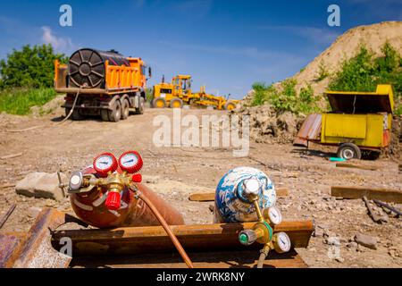 Rote und blaue Schweißgeräte, Sauerstoff- und Stickstofftanks mit Ventilen und Manometern, Acetylengaszylinder auf Metallstapeln im Gebäude Stockfoto