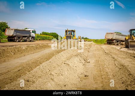 Der Erdbeweger mit caterpillar bewegt auf der Baustelle geparkte Lkw und ein weiterer Planierraupen stehen im Hintergrund. Stockfoto