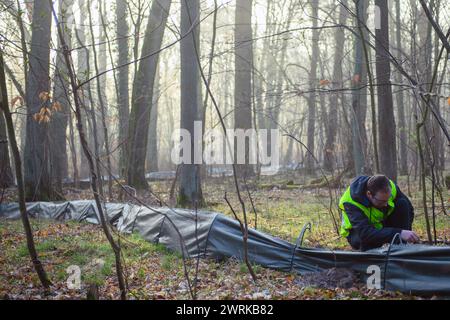 13. März 2024, Sachsen-Anhalt, Ramstedt: Kevin Trawiel, ein Freiwilliger des Deutschen Natur- und Biodiversitätsbundes (NABU), spaziert entlang eines Krötenzauns in einem Wald bei Ramstedt. Er sammelt dort Amphibien, um sie über eine Straße zu einem Laichplatz zu bringen. In Sachsen-Anhalt hat die Amphibienwanderung ihren Höhepunkt bereits überschritten. Aufgrund des milden und nassen Wetters im Februar hatten Mitarbeiter und Freiwillige bereits am 17. Februar 2024 in Ramstedt den Krötenzaun errichtet. 2023 wurde der Krötenzaun erst am 13. März 2023 errichtet. Der Höhepunkt der Amphibienwanderung im Jahr 2023 war der 20. März mit 111 Stockfoto