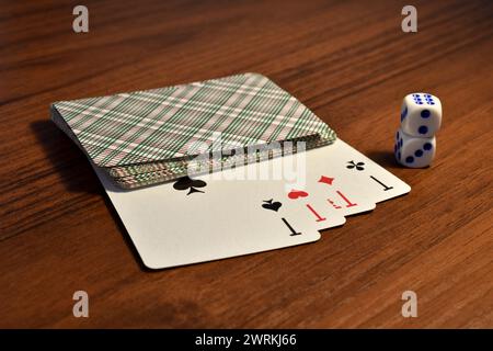 Vier Asse aus einem Kartenspiel, offen und Würfel stehen auf dem Tisch. Stockfoto