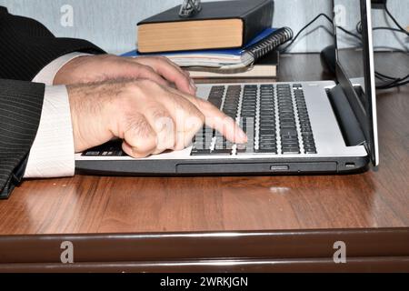 Ein Mann arbeitet an einem Computer und gibt Text auf der Tastatur mit dem Finger ein. Stockfoto